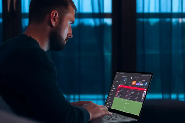 OKPK Mobile App — Your complete hub for casino and sports A man focused on his laptop with live stats in the background, highlighting the dedicated sports and gaming features of the OKPK mobile app.