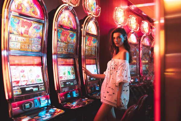OKPK Slots — Thousands of exciting themes and jackpots A stylish woman beside vibrant slot machines displaying glowing sevens, showcasing the variety of top slots at OKPK.