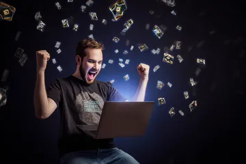 A man celebrating a winning moment on his laptop while gaming symbols float around him, capturing the excitement of OKPK games.